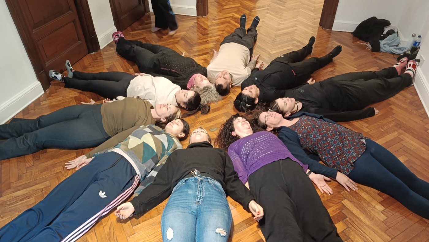 Un grupo acostado en el piso formando un círculo, con las cabezas hacia el centro